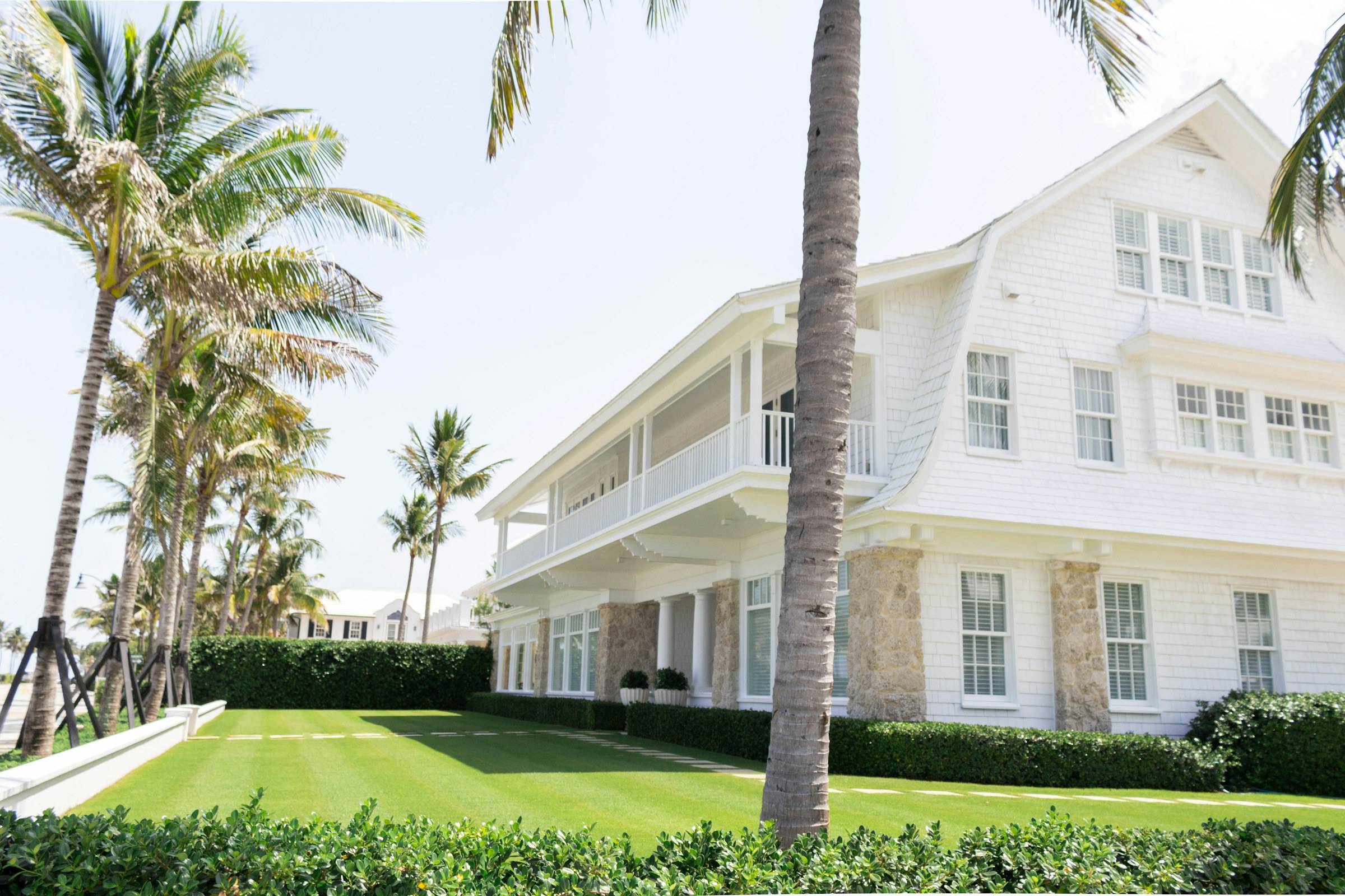 A white shingle-style home with palm trees on a Palm Beach street